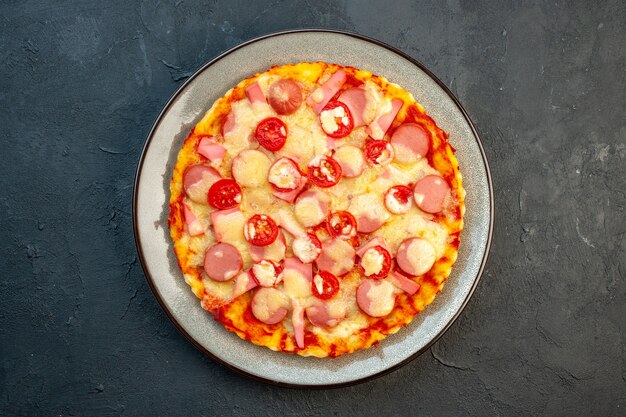 Vista superior de la deliciosa pizza de queso con salchichas y tomates sobre fondo oscuro, comida italiana, pastel de masa, comida rápida, color fotográfico