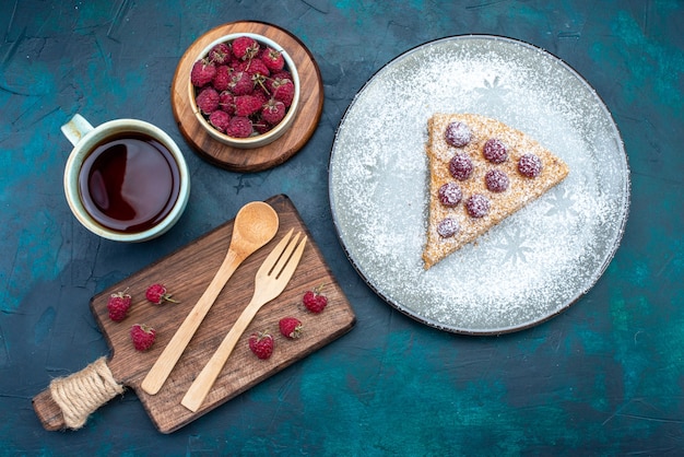 Vista superior de la deliciosa rebanada de pastel con frutas y taza de té de azúcar en polvo sobre una superficie oscura