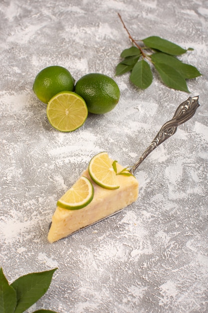 Vista superior de la deliciosa rebanada de pastel con trozos de limón y limas frescas en el fondo claro pastel de azúcar dulce para hornear masa