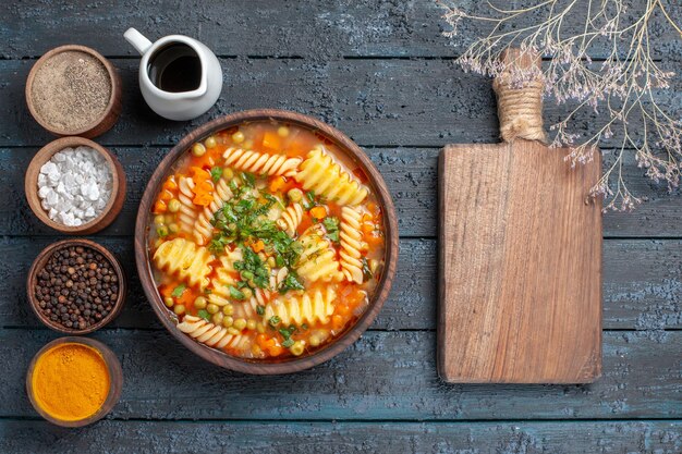 Vista superior de la deliciosa sopa de pasta de pasta espiral con condimentos en el plato de cocina de salsa de escritorio azul oscuro sopa de pasta italiana