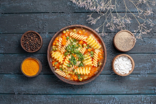 Vista superior de la deliciosa sopa de pasta de pasta espiral con condimentos en el plato de cocina de salsa de escritorio azul oscuro sopa de pasta italiana