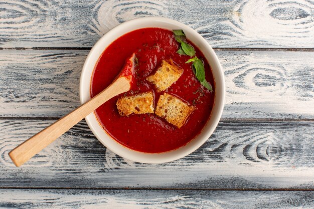 Vista superior deliciosa sopa de tomate con bizcochos en el interior sobre la mesa gris, cena de comida de sopa