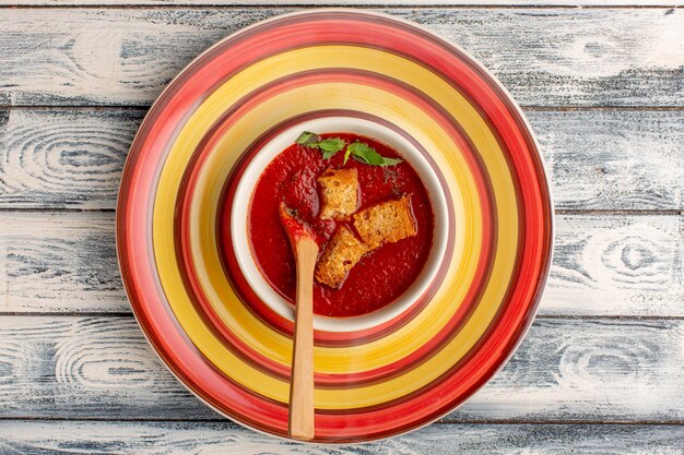 Vista superior deliciosa sopa de tomate con bizcochos en el interior sobre una mesa rústica gris, sopa de cena de verduras