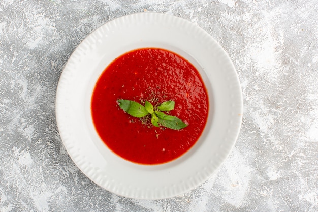 Vista superior deliciosa sopa de tomate con condimentos en mesa gris, cena de sopa de verduras