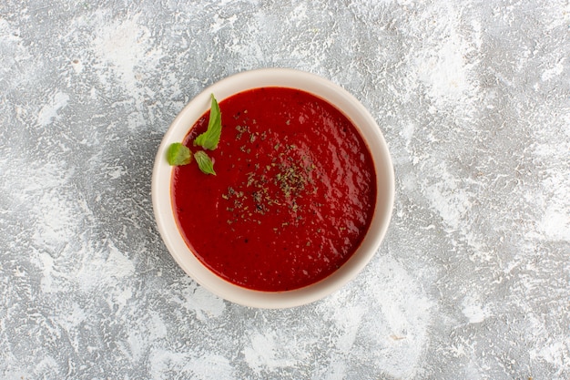 Vista superior deliciosa sopa de tomate con condimentos en mesa gris, cena de sopa de verduras