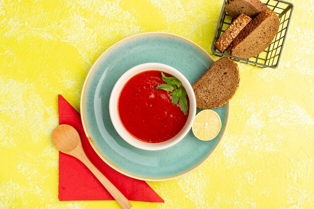 Vista superior deliciosa sopa de tomate con hogazas de pan en la mesa amarilla, comida de sopa cena vegetal