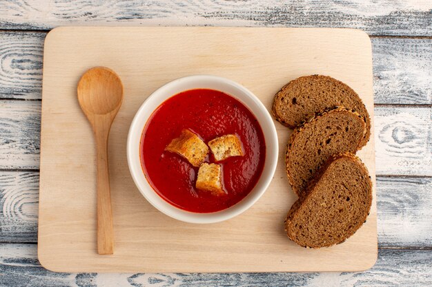Vista superior deliciosa sopa de tomate con hogazas de pan oscuro en la mesa gris, cena de comida de sopa
