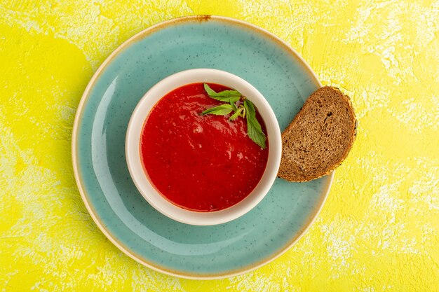 Vista superior deliciosa sopa de tomate con pan en la mesa amarilla, cena de comida de sopa