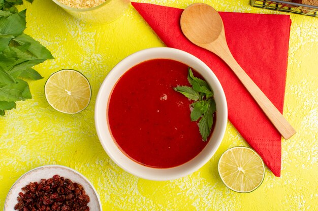 Vista superior deliciosa sopa de tomate con verduras y limón en la mesa amarilla, cena de sopa de verduras