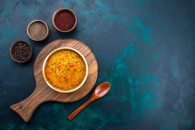 Vista superior deliciosa sopa de verduras dentro de un plato redondo con condimentos en el escritorio azul oscuro.