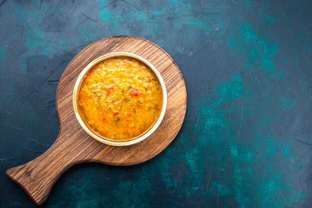 Vista superior deliciosa sopa de verduras dentro de un plato redondo sobre el escritorio azul oscuro.