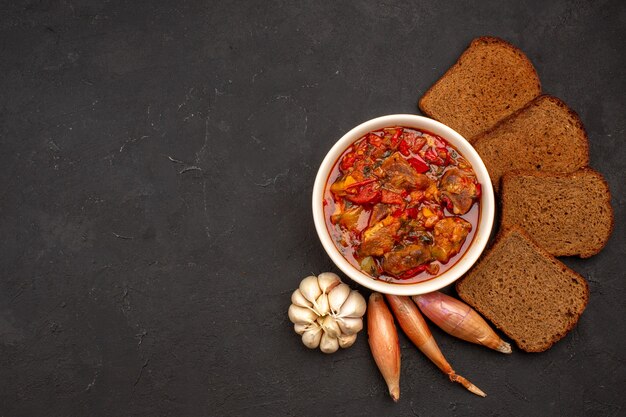 Vista superior deliciosa sopa de verduras con hogazas de pan oscuro en la oscuridad