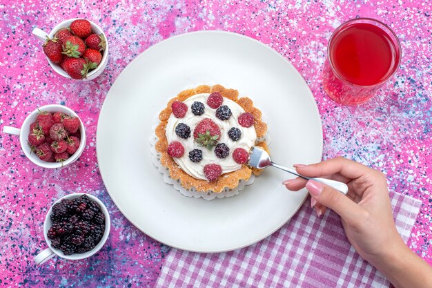 Vista superior de una deliciosa tarta cremosa con diferentes zumos de bayas frescas en un escritorio con luz brillante, fruta de baya agria fresca