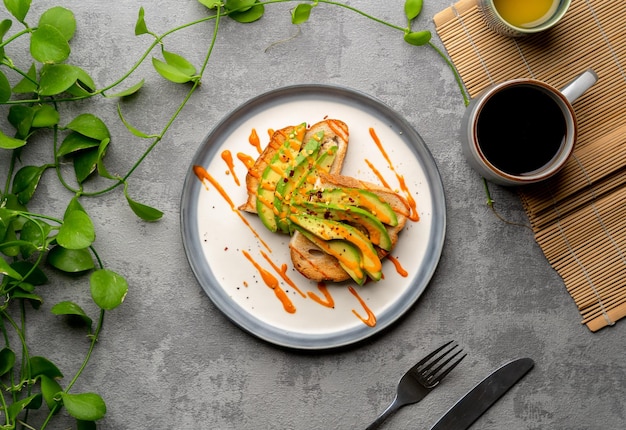 Vista superior de una deliciosa tostada de aguacate cubierta con salsa picante, una taza de café y plantas