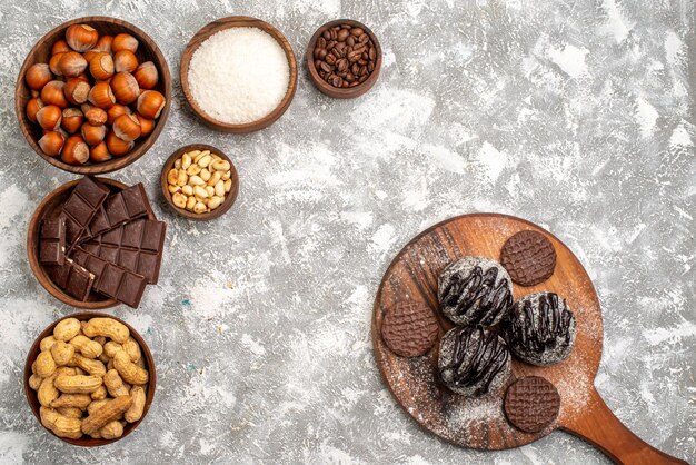 Vista superior de deliciosas barras de chocolate con avellanas y cacahuetes sobre superficie blanca