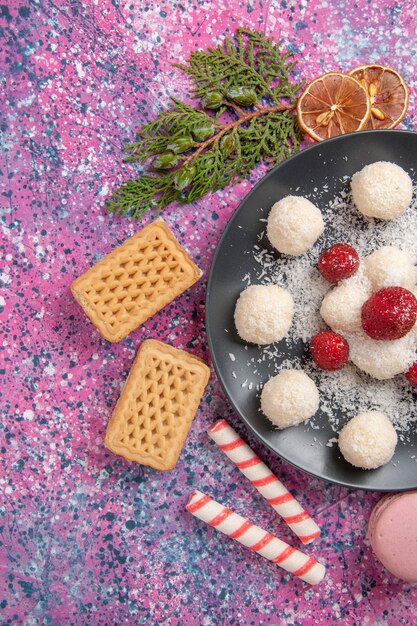 Vista superior de deliciosas bolas dulces de caramelos de coco con gofres y macarons en superficie rosa