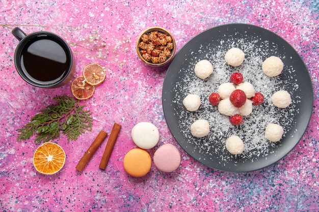 Vista superior de deliciosas bolas dulces de caramelos de coco con macarons franceses en el escritorio rosa