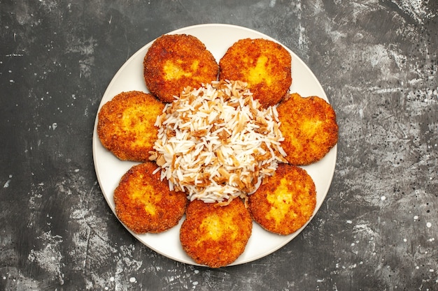 Vista superior deliciosas chuletas fritas con arroz cocido en la comida de la foto del plato de carne de superficie oscura