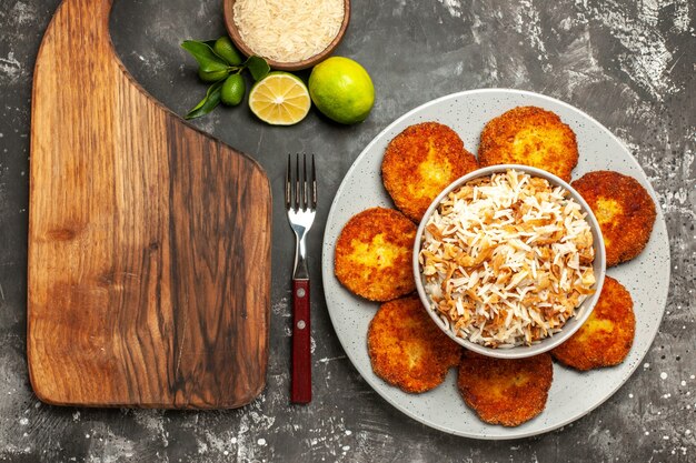 Vista superior deliciosas chuletas fritas con arroz cocido en un plato de carne rissole de superficie oscura