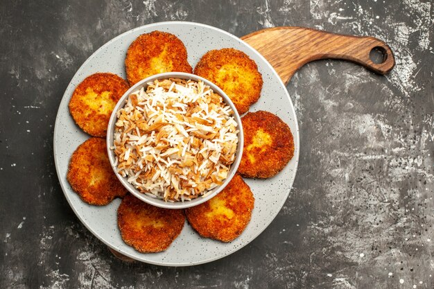 Vista superior deliciosas chuletas fritas con arroz cocido en un plato de superficie oscura rissole de carne