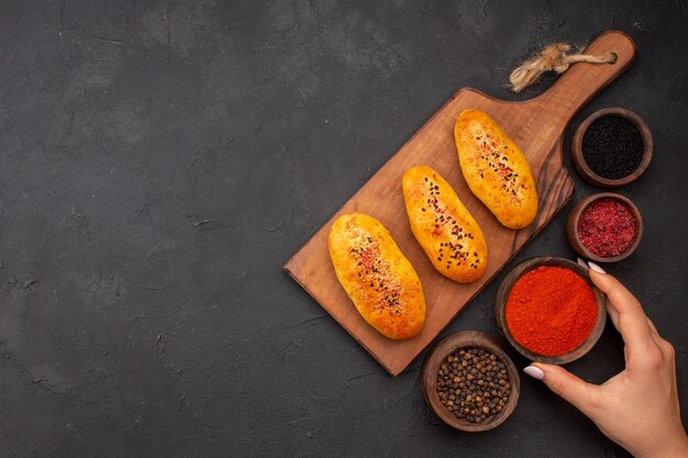 Vista superior deliciosas empanadas al horno recién salido del horno con condimentos en el fondo gris horno de pastel de carne pastelería pastel hornear