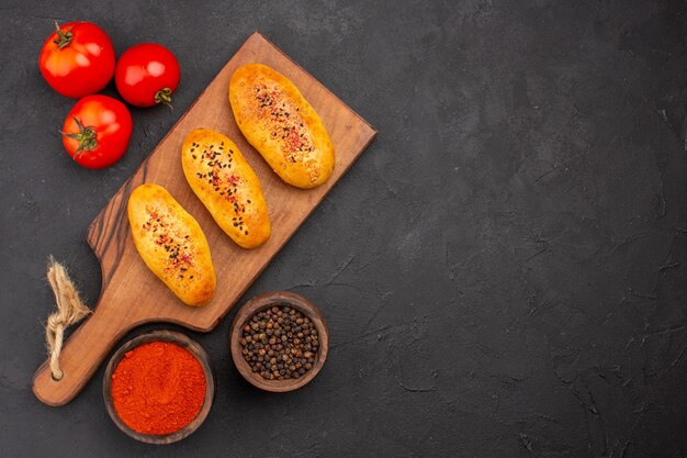 Vista superior deliciosas empanadas al horno recién salido del horno con tomates en el fondo gris horno de tarta masa de pastelería pastel de carne hornear