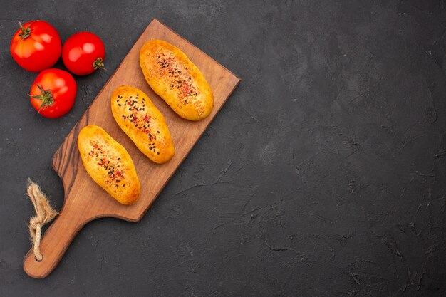 Vista superior deliciosas empanadas al horno recién salido del horno con tomates en el fondo gris horno de tarta masa de pastelería pastel de carne hornear