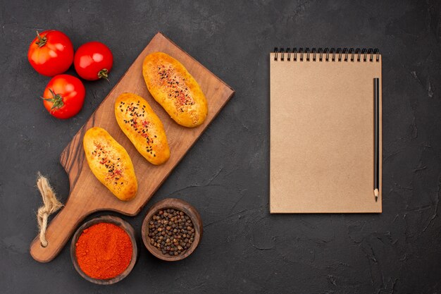 Vista superior deliciosas empanadas al horno recién salido del horno con tomates en el fondo gris horno de tarta masa de pastelería pastel de carne hornear