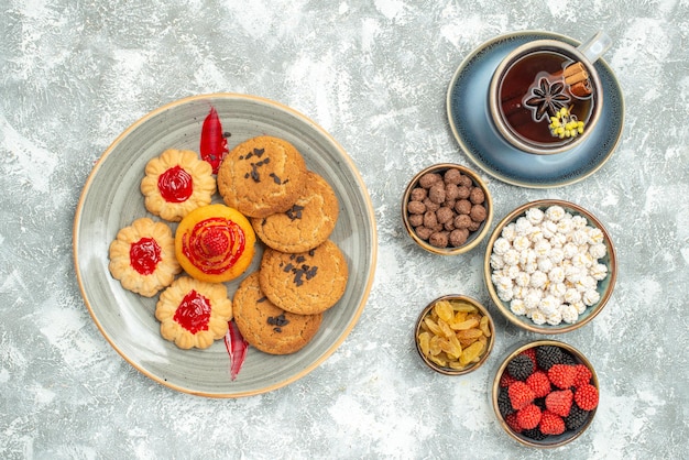 Vista superior deliciosas galletas de arena con galletas dulces y una taza de té sobre fondo blanco galleta de azúcar de té galleta pastel