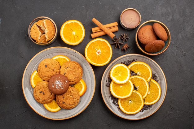 Vista superior deliciosas galletas de arena con naranjas frescas en rodajas sobre fondo oscuro galleta de fruta dulce color cítrico de azúcar de galleta