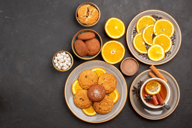 Vista superior deliciosas galletas de arena con naranjas frescas y una taza de té sobre fondo oscuro galleta de fruta galleta dulce azúcar cítrico
