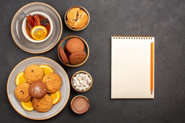 Vista superior deliciosas galletas de arena con naranjas en rodajas y una taza de té sobre fondo oscuro galletas cítricas de frutas pastel dulce galletas