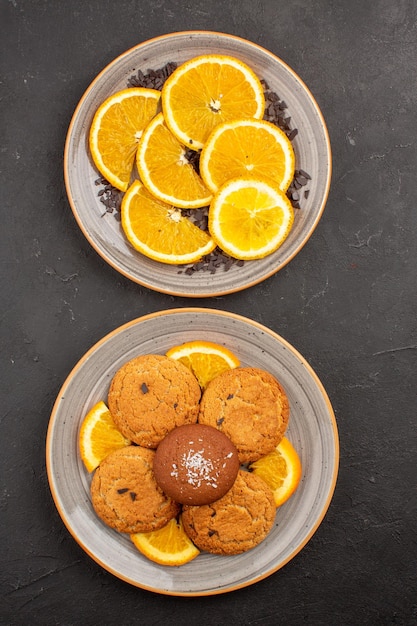 Vista superior deliciosas galletas de azúcar con naranjas frescas en rodajas en el escritorio oscuro galleta de azúcar fruta dulce galleta