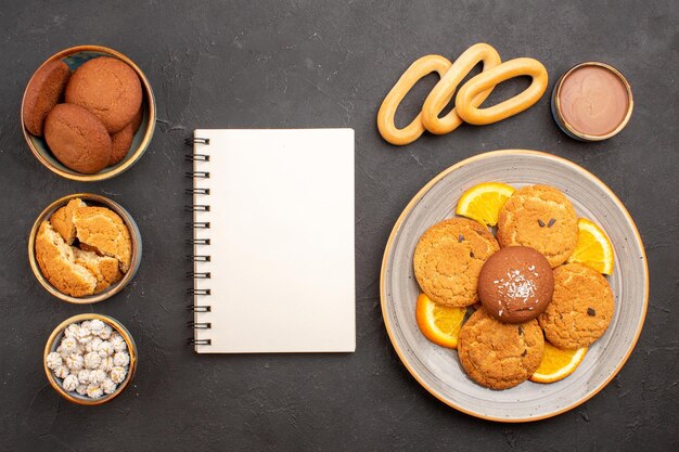 Vista superior deliciosas galletas de azúcar con naranjas frescas en rodajas sobre el fondo oscuro galletas galleta postre pastel de azúcar dulce