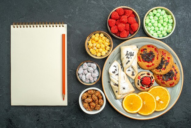 Vista superior deliciosas galletas de azúcar con pasteles, dulces y rodajas de naranja en la superficie oscura galleta de azúcar pastel de té de galletas dulces