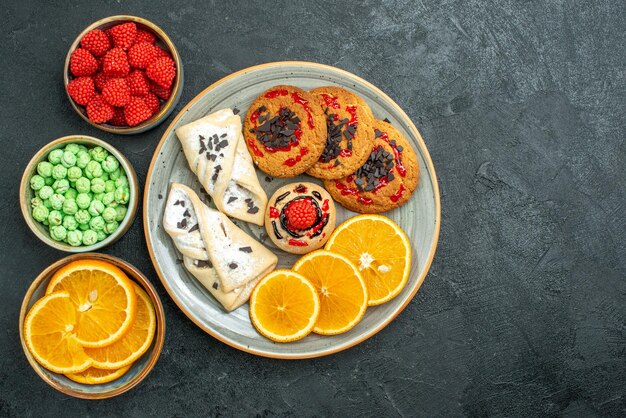 Vista superior de deliciosas galletas de azúcar con pasteles y rodajas de naranja sobre la superficie oscura de azúcar galleta dulce pastel galletas té