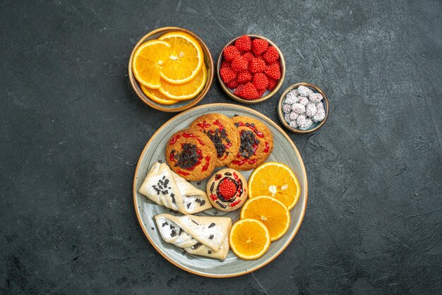 Vista superior de deliciosas galletas de azúcar con pasteles y rodajas de naranja sobre la superficie oscura de azúcar galleta dulce pastel de té de galleta