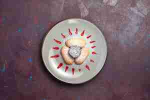 Foto gratuita vista superior de deliciosas galletas con azúcar en polvo y glaseado rojo dentro de la placa en la oscuridad