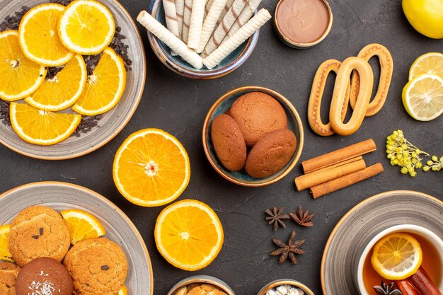 Vista superior deliciosas galletas de azúcar con taza de té y naranjas sobre fondo oscuro azúcar té fruta galleta galleta dulce