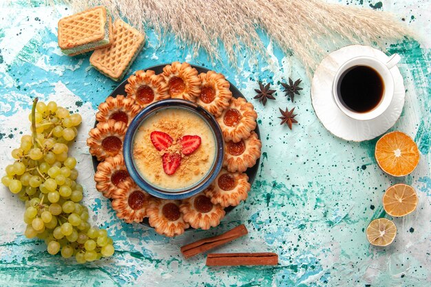 Vista superior deliciosas galletas de azúcar con taza de waffles de uvas de café y postre de fresa en el escritorio azul