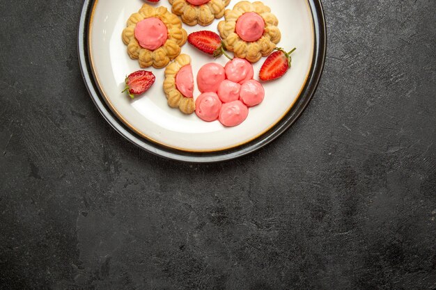 Vista superior de deliciosas galletas con crema rosa dentro de la placa sobre superficie gris