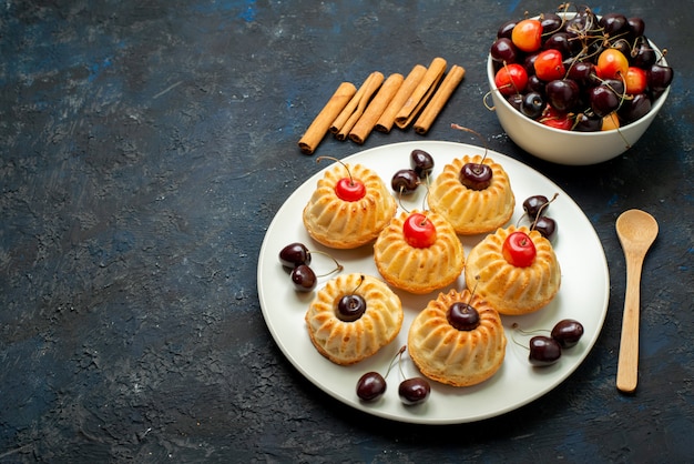 Una vista superior deliciosas galletas dentro de la placa blanca con cerezas en el fondo oscuro pastel de galletas de frutas