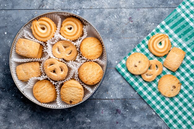 Vista superior de deliciosas galletas diferentes formadas dentro del paquete redondo en el escritorio gris, galleta de pastel de azúcar dulce