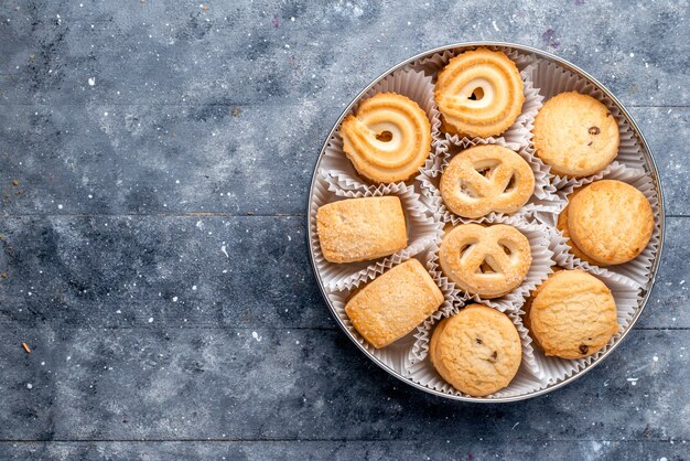 Vista superior de deliciosas galletas dulces diferentes formados dentro del paquete redondo en el escritorio gris galleta de pastel dulce galleta