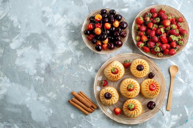 Una vista superior deliciosas galletas con fresas rojas cerezas dentro de placas en el escritorio oscuro galleta cookie