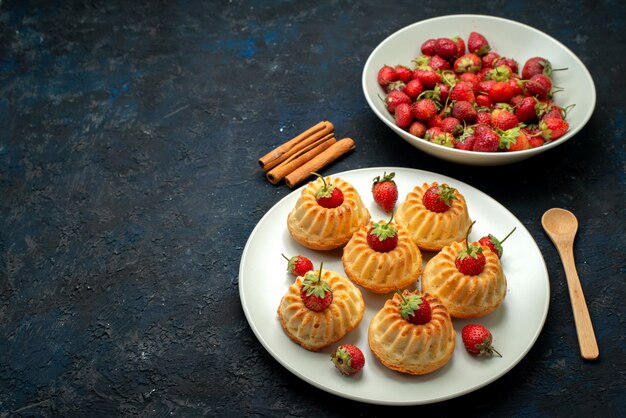 Una vista superior deliciosas galletas con fresas rojas dentro de la placa blanca en la galleta de escritorio oscuro