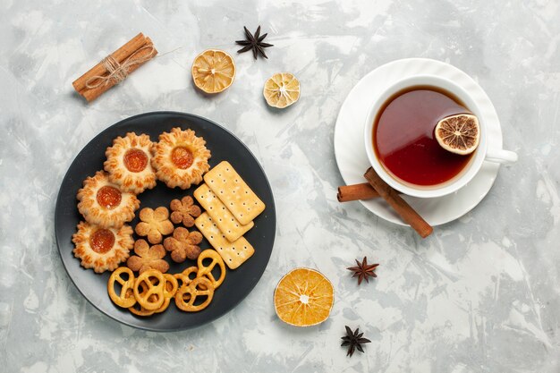 Vista superior deliciosas galletas con galletas saladas y patatas fritas dentro de la placa con una taza de té en el escritorio blanco claro galleta galleta azúcar té dulce crujiente