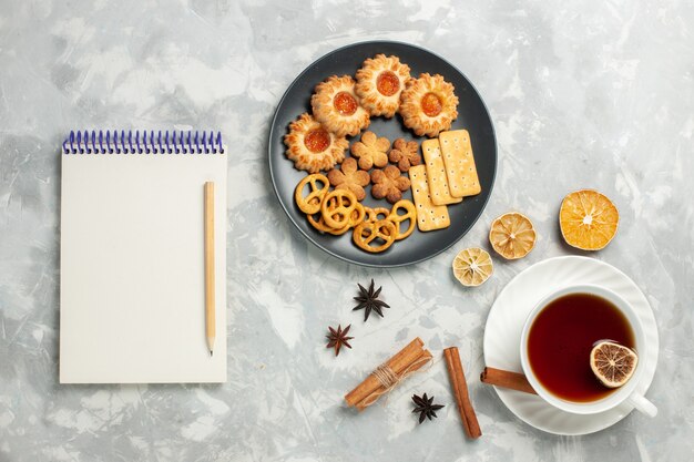 Vista superior deliciosas galletas con galletas saladas y patatas fritas dentro de la placa con una taza de té en el escritorio blanco claro galletas galletas azúcar té dulce patatas fritas