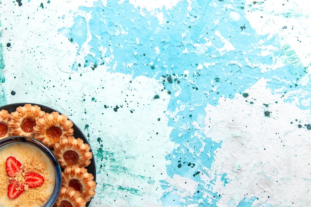 Vista superior deliciosas galletas con mermelada y postre de fresa en el pastel de galleta dulce de azúcar de galleta de fondo azul claro
