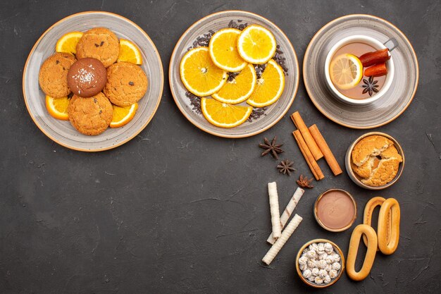 Vista superior deliciosas galletas con naranjas en rodajas y una taza de té sobre fondo oscuro galleta de azúcar galleta dulce de frutas